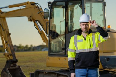 İnşaat alanındaki bir inşaatçının portresi. Kazıcı yeni bir ev inşa etmeye hazır. İnşaat işçileri kazı kamyonu kazılarında inşaat üniforması giyerler, inşaat işlerinde çalışırlar.