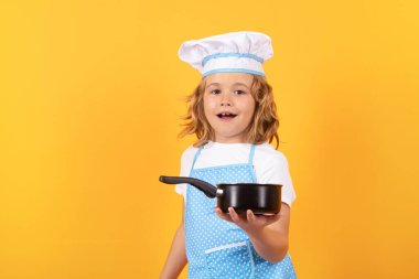 Aşçı çocuk tencereyle yemek pişiriyor. Aşçı çocuk sağlıklı yemek yapıyor. Stüdyo arka planında izole edilmiş, şef şapkalı küçük çocuk portresi. Çocuk aşçı. Yemek pişirme süreci