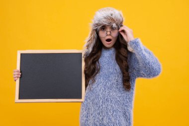 Kara tahtalı, kışlık şapkalı küçük bir kız. Liseli kız fotokopi odası ve okul satışı için karatahta tutuyor. Genç bir kız öğrencinin portresi. Şaşırmış yüz, genç kızın sürprizi.