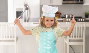 Aşçı çocuk mutfakta yemek yapıyor. Çocuk aşçı mutfakta yemek hazırlar. Çocuklar yemek yapıyor. Önlüğü ve aşçı şapkası olan genç çocuk sağlıklı bir yemek hazırlıyor.