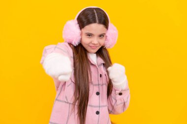 Saldırgan çocuk kürklü kulaklıkları yumrukluyor. Sarı arka planda kadın manken. Eldivenli genç kız. Kalın giysiler giyen çocuk portresi. Duygularını ifade et. kış modası.