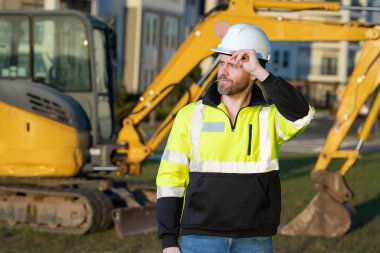 İnşaat alanında çalışan bir işçi. Şapkalı bir inşaatçı. Kasklı bir inşaat işçisi. Miğferli inşaat işçisi. İnşaat binasında sanayi işçisi. İnşaatçı, kazıcıyla birlikte inşaat alanında.