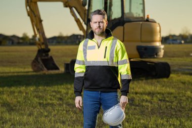 İnşaat alanındaki bir inşaatçının portresi. Kazıcı yeni bir ev inşa etmeye hazır. İnşaat işçileri kazı kamyonu kazılarında inşaat üniforması giyerler, inşaat işlerinde çalışırlar.