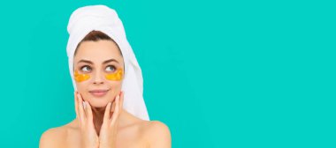 Güzel yüzlü kadın, yüz portresi. Gülümseyen genç kadının yüzünde havluyla kolajen altın göz bantları var. Güzel kadın, izole edilmiş yüz portresi, taklit alanı olan pankart.