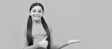 Portakal rengi arka planda fotokopi çeken mutlu genç kız başparmağını kaldır ve ürün teklifini yap. Çocuk yüzü, yatay poster, izole edilmiş genç kız portresi, fotokopi alanı olan pankart