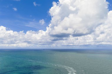 Ufuktaki sakin denizin yanında mavi gökyüzü. Okyanusun üzerinde bulutlar olan manzaralı deniz manzarası. Güneşli bir gökyüzünün altında huzurlu bir kıyı şeridi. Bulutlu gökyüzü denize yansıyor. Bulutlu yaz gökyüzü kıyısı. Bulutlu okyanus manzarası