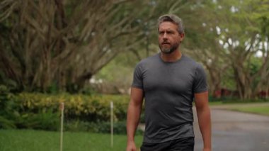 Spordan sonra yürüyen bir sporcu. Açık havada spor giyinen olgun bir adam. İspanyol sporcu antrenmandan sonra hızlı yürür. Spor ve sağlıklı yaşam tarzı. Spor kıyafetleri. Yürüyen adam.
