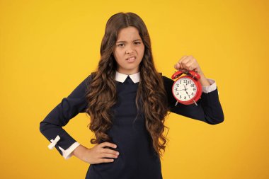 Saati, zamanı ve son teslim tarihi olan genç bir kızın portresi. Stüdyo çekimi sarı arkaplanda izole edildi. Kızgın genç kız, üzgün ve mutsuz negatif duygu.