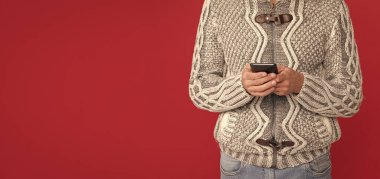 Gülümseyen erkek manken akıllı telefonu tut. Modern iletişim kavramı. Kırmızı arka planda kazaklı ve şapkalı kır saçlı adam. Beyaz adam telefonda konuşuyor..