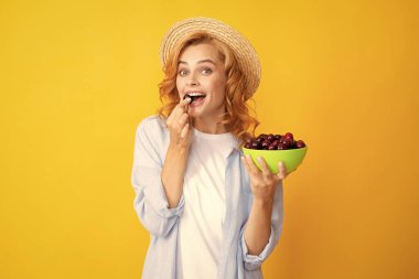 Attractive young woman eating fresh cherry. Healthy summer fruits. Picking eating cherry fruit. Yellow background. Beautiful woman posing with a cherry, girl with cherry promoting