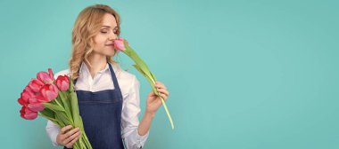 girl smile in apron with spring tulip flowers on blue background. Woman isolated face portrait, banner with mock up copy space