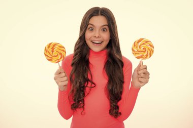 Şekerli lolipop yiyen genç bir kız. Çocuklar için şeker ve şeker. Çocuk beyaz izole arka planda lolipop yiyor. Lezzetli karamel, şekerci dükkanı. Mutlu kız yüzü