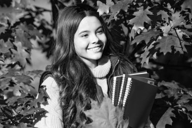 Sonbahar çocuk portresi. Mutlu kız sonbahar yaprakları üzerine çalışma kitabı tutuyor..