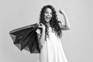 Sarı arka planda alışveriş torbaları olan güzel moda kızı. Alışveriş ve moda alışverişi. Alışveriş çantalı çocuk. Heyecanlı bir genç, şaşkın ve neşeli duygular içinde