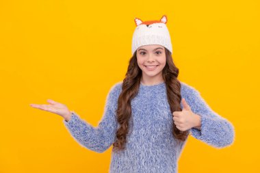 Sarı arka planda süveter ve şapka giyen mutlu çocuk, çocukluk.