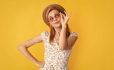 Sarı arka planda hasır şapkalı ve güneş gözlüklü neşeli kadın..