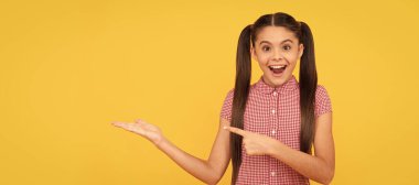 surprised teen girl pointing finger on yellow background copy space, advertisement. Child face, horizontal poster, teenager girl isolated portrait, banner with copy space