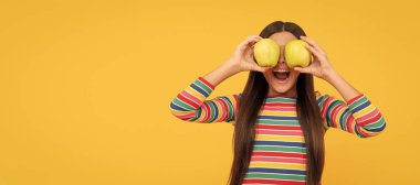 Mutlu kız çocuğu, sarı arka planda elma meyvesi tutarken, göz sağlığında iyi eğlenceler. Elmalı çocuk portresi, yatay poster. Kopyalama alanı olan başlık