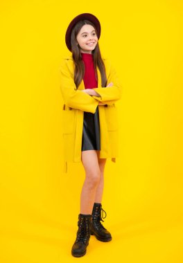 Uzun boylu, çekici, sevimli, neşeli, güler yüzlü, sonbahar ceketli, sarı arka planda izole bir genç kız çocuğu. Mutlu ergen portresi. Gülümseyen kız