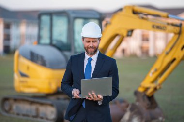 Kazıcının yanında inşaat işçisi. Evin önünde kendine güvenen bir inşaat sahibi. Mimar, inşaat mühendisi. İnşaat alanında güvenlik yeleği ve kasketi olan bir inşaat sahibi.