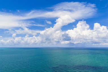 Ufuktaki sakin denizin yanında mavi gökyüzü. Okyanusun üzerinde bulutlar olan manzaralı deniz manzarası. Güneşli bir gökyüzünün altında huzurlu bir kıyı şeridi. Bulutlu gökyüzü denize yansıyor. Bulutlu yaz gökyüzü kıyısı. Bulutlu okyanus manzarası