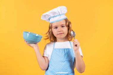 Aşçıbaşı aşçı çocuk. Çocuk pişirme, küçük şef yemek hazırlıyor. Sarı stüdyodaki aşçı şapkalı ve önlüklü çocuk izole edilmiş.