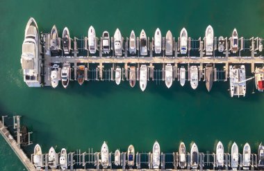 Miami marinası boyunca lüks bir yat ve tekne manzarası. Turkuaz tropikal sularda beyaz bir yatın hava görüntüsü. Seçkin bir yat. Canlı bir marinada yatlar. Lüks yatlar gezisi
