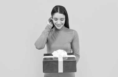 smiling girl holding gift box after shopping on yellow backdrop, purchase.