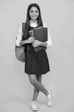 Okul çantalı genç kız sarı izole edilmiş stüdyo geçmişi üzerine kitap tutuyor. Çocuk okulu ve eğitim konsepti