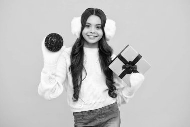 Yeni yıl ya da Noel hediyesi. Sarı stüdyo arka planında izole edilmiş hediye kutusunu tutan genç bir kızın portresi. Hediye, selam ve hediye konsepti. Doğum günü tatili kavramı