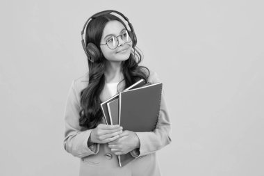 Young american girl teen student with headphones and books isolated on yellow background studio portrait. Education in school college