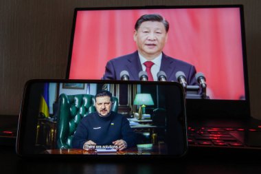 Kyiv, Ukraine - March 16 2023: Ukrainian President Volodymyr Zelenskyy on the phone screen from the presidency, Chinese President Xi Jinping in the background. clipart