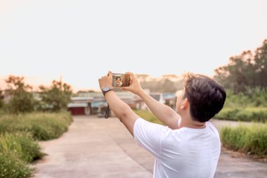 Kendisinin ve doğanın çeşitli şekillerde fotoğraflarını çeken bir adam. Adamın sırtı kameraya dönük. Güneşli bir öğleden sonra doğada.