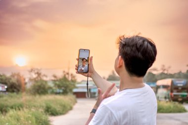 a man who is taking photos of himself and nature in various styles. the man has his back to the camera. set on a sunny afternoon in nature. clipart