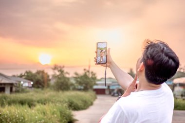 Kendisinin ve doğanın çeşitli şekillerde fotoğraflarını çeken bir adam. Adamın sırtı kameraya dönük. Güneşli bir öğleden sonra doğada.