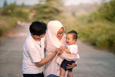 Anne, baba ve oğlanla bol bol kahkaha atan bir aile. Onlar erkek bebeğe sataşırken güldüler. Baba ve anne çocuğu görünce gülümsüyor. doğadaki fotoğraf atmosferi.