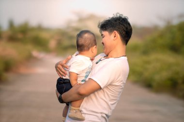 Babam bebeğe içtenlikle gülümsedi. Baba kucağında ve kucağında bebeğiyle evin dışında. Öğleden sonra doğal atmosferin arka planı.