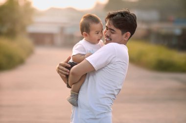 Baba, bebeği sımsıkı tutuyor ve gülümsüyor. Erkek bebek diğer yönde sevimli bir gülümseme takındı..