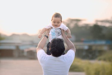 Baba kucağında bebek taşırken. Babamın sırtı kameraya dönük. Fotoğraf öğleden sonra açık havada çekildi..