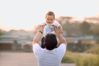 Baba kucağında bebek taşırken. Babamın sırtı kameraya dönük. Fotoğraf öğleden sonra açık havada çekildi..