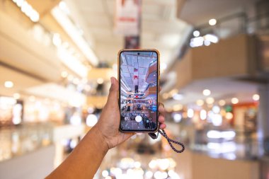 Adam akıllı telefonuyla alışveriş merkezinin fotoğrafını çekiyor. Adam cep telefonuyla etrafındaki nesnelerin fotoğrafını çekerken görülüyor. Portre sonuçları çok net ve iyi..