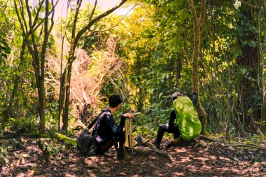 Sırt çantalı iki Maceraperest Yürüyüşçü dağa çıkıyor. Yürüyüşçü Oturuyor ve Manzarayı Özümsüyor.