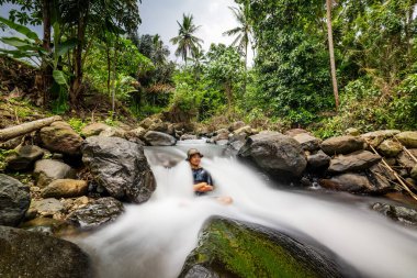 Huzurlu bir nehirde ferahlatıcı bir dalışın tadını çıkaran adam. Kristal berrak suları ve bereketli çevresiyle Manzaralı Nehir Manzarası.