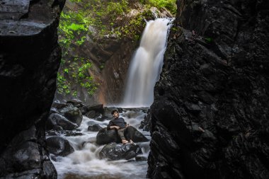 Yakışıklı adam güzel şelalenin önündeki kayada dinleniyor..