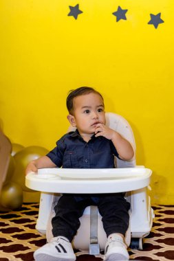 Yüksek sandalyesinde oturan sevimli, sevimli erkek bebek. Tatlı çocuk parmağını tatlı bir poza sokuyor.