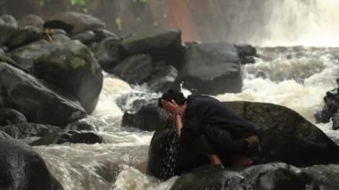 Adam vahşi doğada yüzünü ağır çekim 4K ile yıkıyor. Kayalıkları olan ve vahşi doğada hızla akan bakire bir nehir.