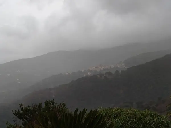 Deniz Dağı Gökkuşağı manzarası Marciana villaları bulutlu bir gün Elba Adası İtalya Yağmurdan sonra Livorno Puslu atmosfer Tropikal dağlık kırsal kasaba tepe manzaralı orman tepe üzerindeki sis bulutu