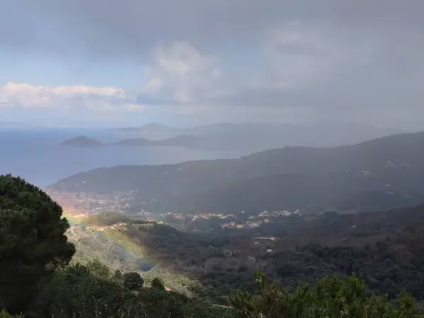 Elba Adası üzerindeki gökkuşağı İtalya sisli deniz dağları antik Livorno köyü yeşillik içinde yuva yapmış. Yağmurdan sonra sisli atmosfer manzaralı tropikal dağlar tropikal manzara bulutlu bir gün