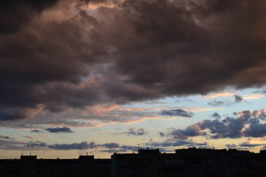 Parlak alışılmadık gün batımı şehir manzarası turuncu pembe ışınlar şehrin üzerinde. Acımasız panel binalar, koyu yağmur fırtınası bulutlarını aydınlatan turuncu-sarı ateşli gökyüzüne karşı siyah siluetler gibi görünür.