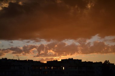 Parlak alışılmadık gün batımı şehir manzarası turuncu pembe ışınlar şehrin üzerinde. Acımasız panel binalar, koyu yağmur fırtınası bulutlarını aydınlatan turuncu-sarı ateşli gökyüzüne karşı siyah siluetler gibi görünür.